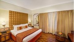 Deluxe King Room at Pride Premier Pune featuring a plush bed and a couple of nightstands on both sides with lamps above them