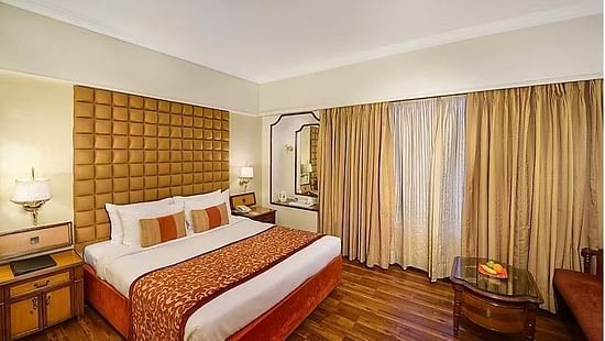 Deluxe King Room at Pride Hotel Pune featuring a plush bed and a couple of nightstands on both sides with lamps above them