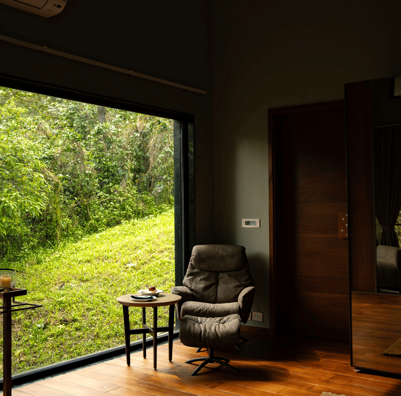 A comfortable armchair and a small table sit near a large window overlooking a lush green field at Stanley Revelation.
