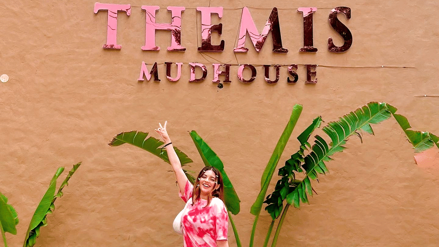 a woman with her luggage standing in front of Themis Mudhouse - A Nature's Retreat Resort & Wellness