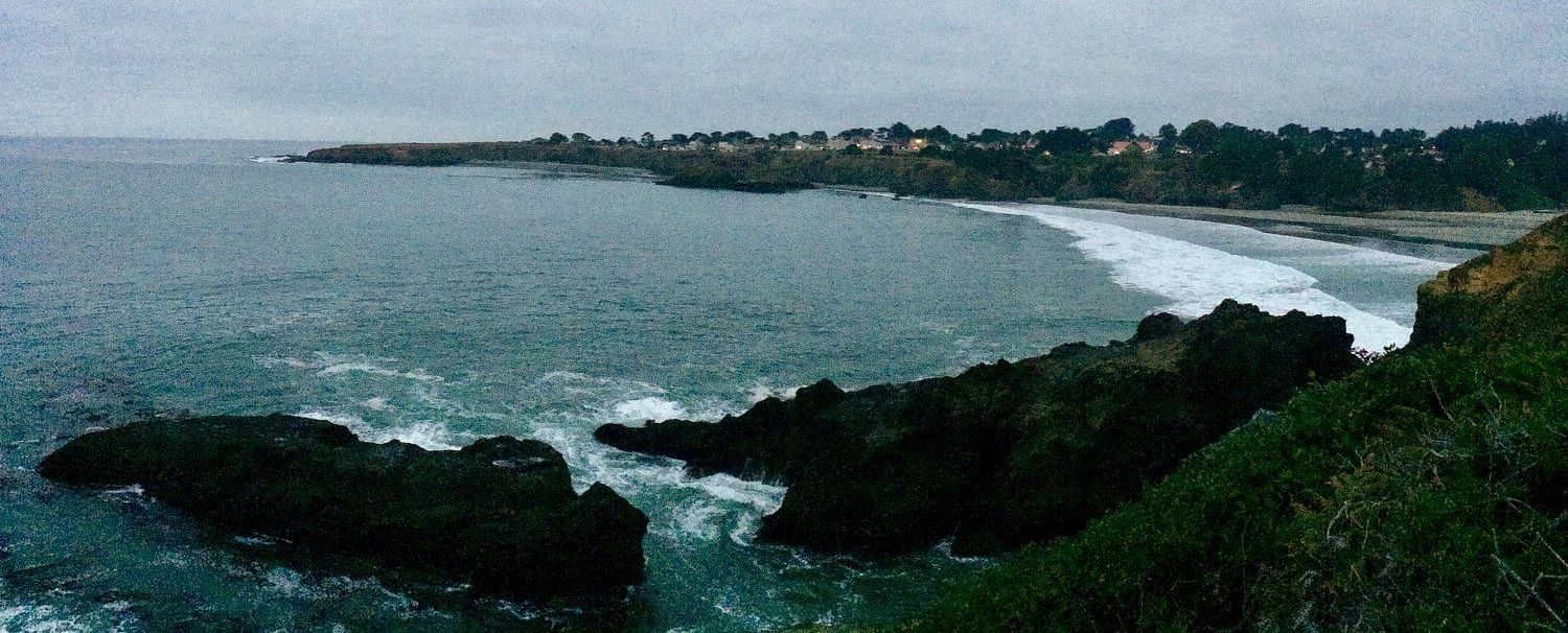 A scenic coastal view with rocky cliffs, ocean waves, and a cloudy sky in the background.