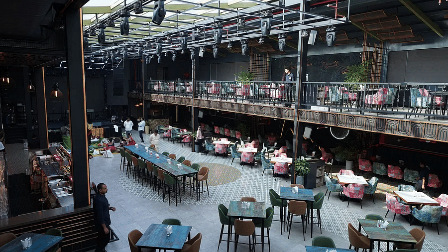 Interior view of a spacious restaurant with a glass ceiling, featuring a mix of seating arrangements, tables, and a vibrant decor, and staff members attending to guests - Clarion Bangalore
