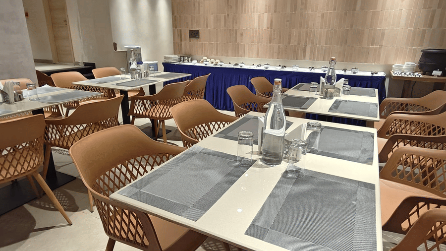 Contemporary restaurant ambience at Hotel Bluestone Prime highlighting neatly set tables, comfortable chairs, air-conditioned interiors, and a wall-mounted television, creating a calm and welcoming environment for everyday dining.