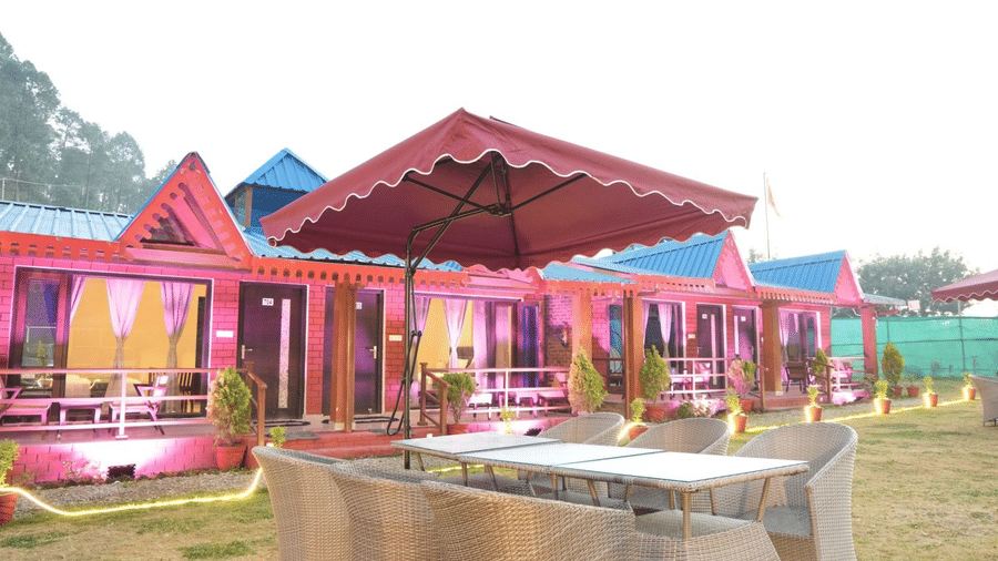 A set of chairs around a table with an umbrella to cover all who are seated, in front of some cottages