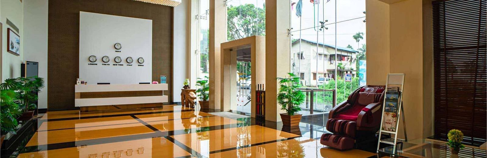 A brightly lit hotel lobby at Mansha Hotel Regency with shiny floors, a reception desk, and large glass windows looking out onto the exterior.