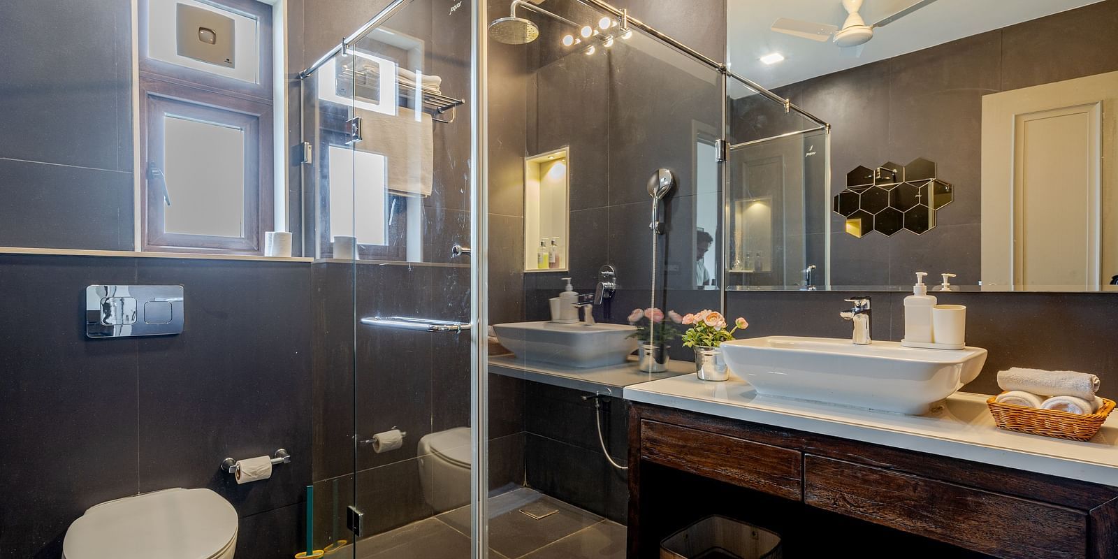 Bathroom at Lindsay Manor with glass-enclosed shower, double sink counter, toilet, and dark wall tiles.