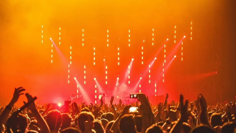 A crowd raises hands enjoying a concert with bright orange stage lights.