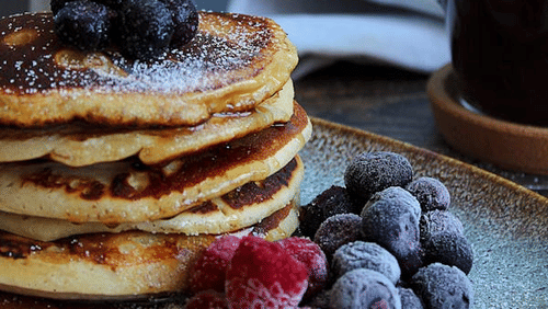 An image of pancakes topped with fruit, served with coffee and a coffee pot.