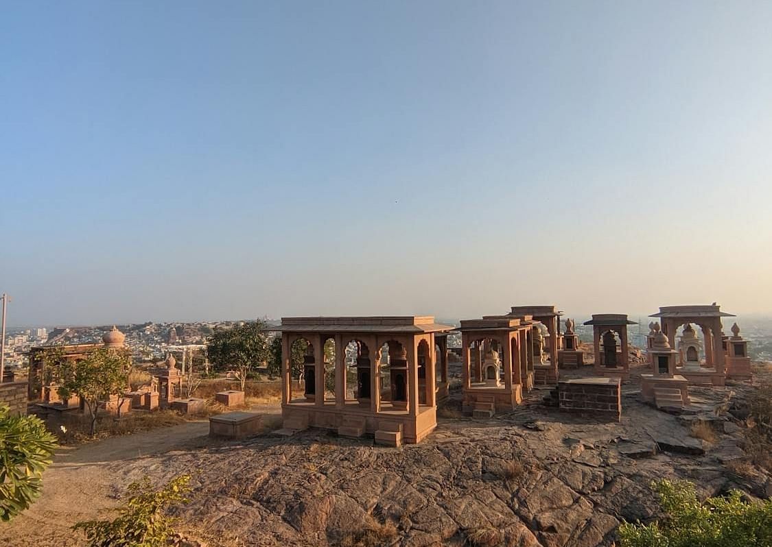 Ancient ruins with stone structures stand on a rocky terrain under a clear sky.