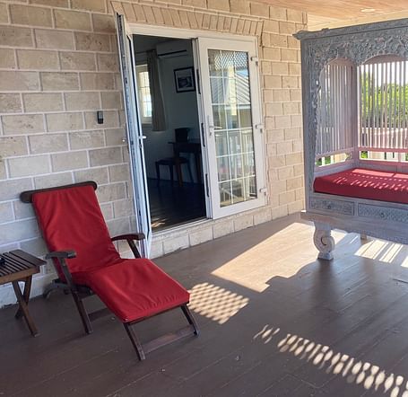 Veranda with red lounge chairs and sunlight streaming through white railing | A Stone's Throw Away