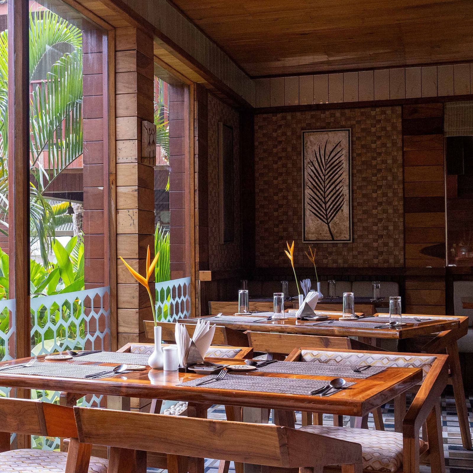 A spacious dining area at Ocean Prime with wooden tables and chairs, set in a modern wooden room. The decor is minimalist, with large windows offering a glimpse of the outside greenery - Coral Reef Resort & Spa, Havelock