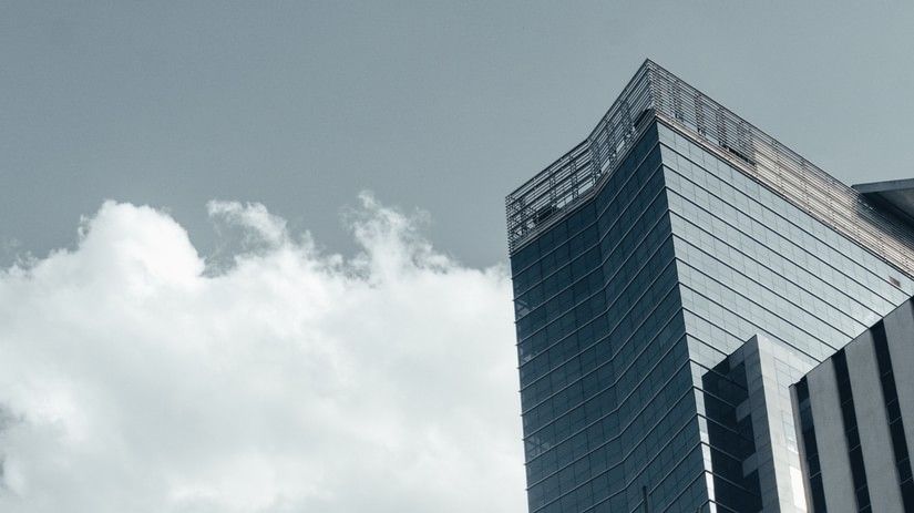 Tall modern glass skyscrapers reflecting the sky and clouds, showcasing sleek contemporary architecture against white clouds in the background
