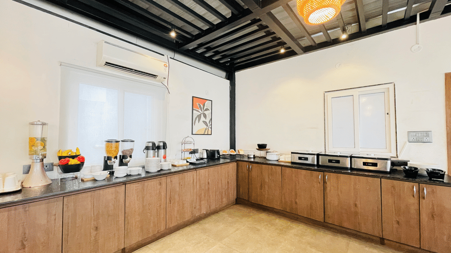 Restaurant buffet counter at Hotel Kyzen Smart Stays Madhapur with wooden cabinetry, dark granite top, food display stations, and pendant lighting under dark ceiling beams.