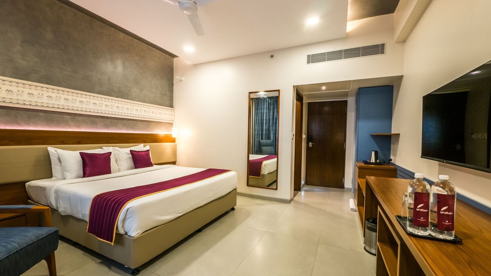  A wide view of a spacious hotel room with a large bed, a desk area, and a television, ready for guests at Shilton Dee Cee.