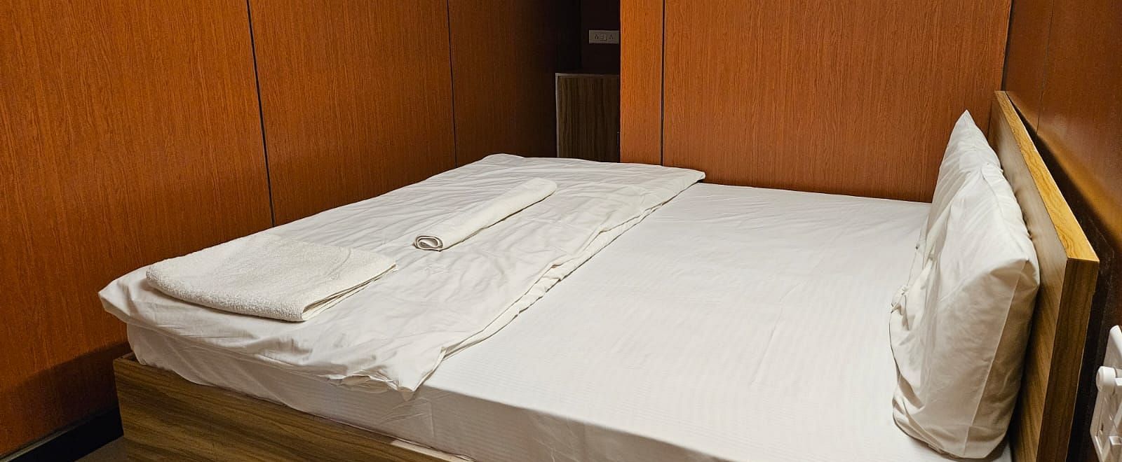 Corner view of a double bed with plain white bed sheet along with a wall mounted television at the Dream Vision Guest House.