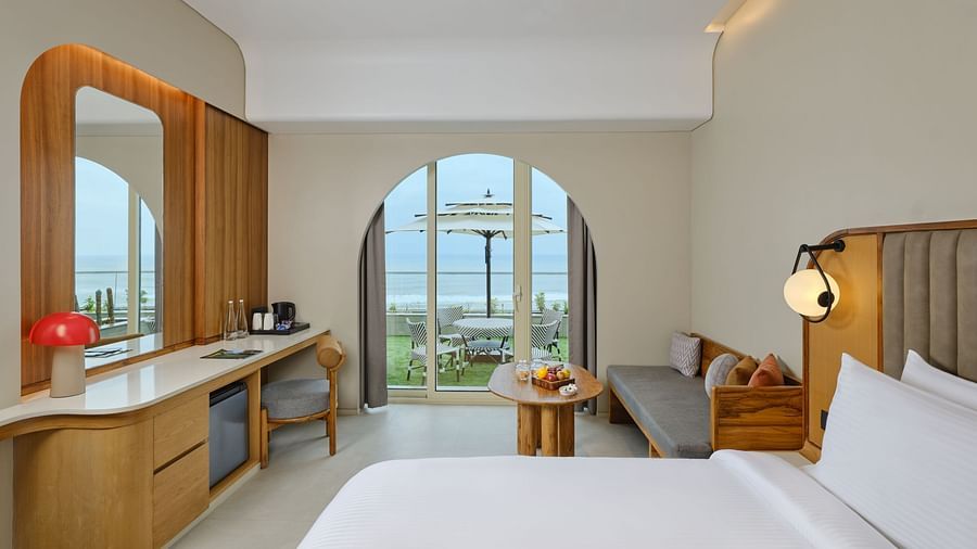 Image of Premium Room at Swosti Premium Beach Resort in Puri featuring a plush bed and a couch with a coffee table next to the doorway to the outdoor sitting space with the majestic view of the sea