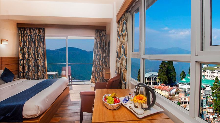 Cosy bedroom with large windows and a balcony overlooking scenic mountains, featuring a welcome tray with fruits and tea essentials - Central Heritage Resort and Spa