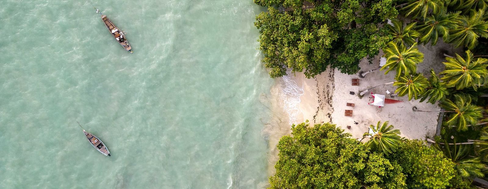 A view of people kayaking in the turquoise waters near a serene beach, surrounded by lush tropical greenery. The peaceful environment adds to the natural beauty of the scene - Coral Reef Resort & Spa, Havelock