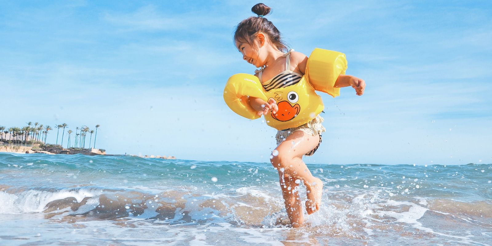 A joyful child wearing floaties playing in the shallow waves at the beach on a sunny day.