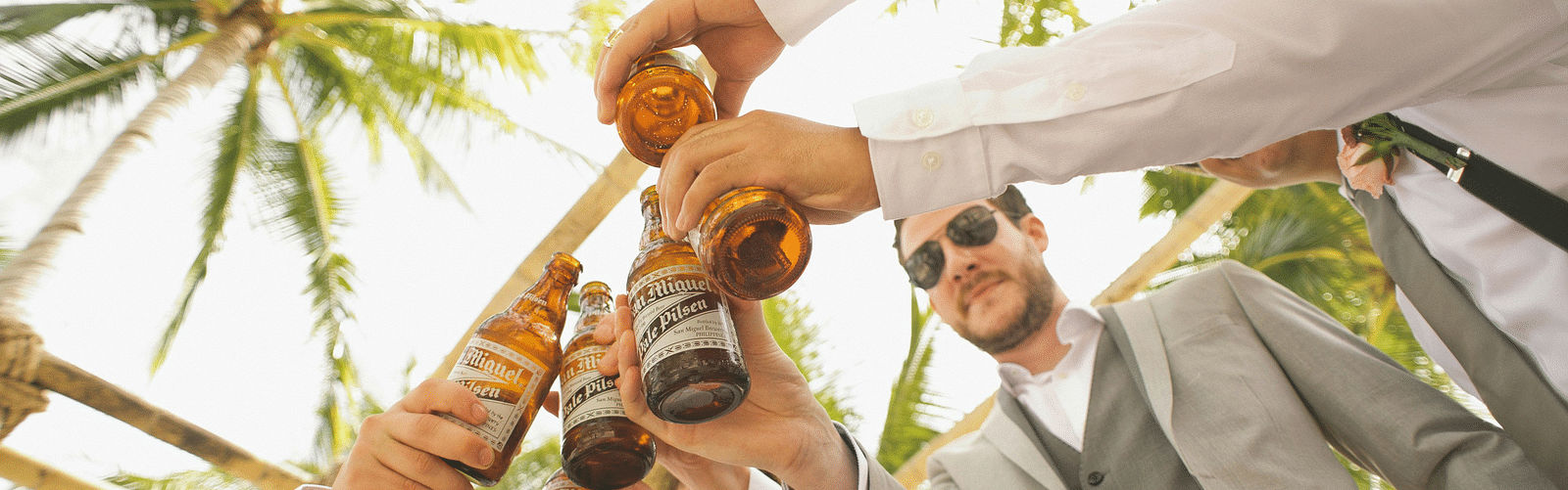 a group of guys toasting their drinks with palm trees above them