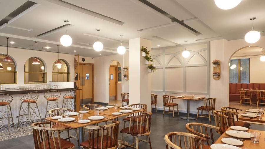 The spacious dining hall at Monday Hotels Mahape, Navi Mumbai, with multiple wooden tables and a central bar.