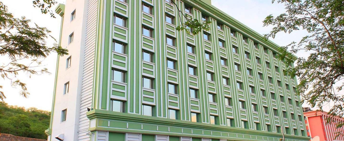 A multi-story green hotel building flanked by trees at Tara, Comfort Hotel in Hyderabad - Ramoji Film City.