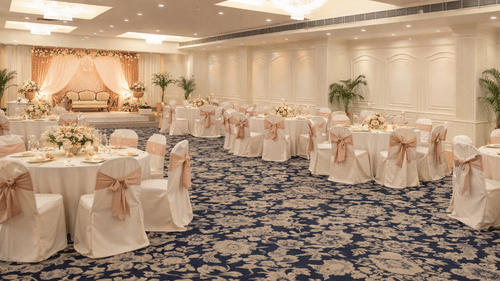 A banquet hall with round tables covered in table linen, banquet chairs, patterned carpeting, and recessed ceiling lighting at Clarks Avadh, Lucknow.