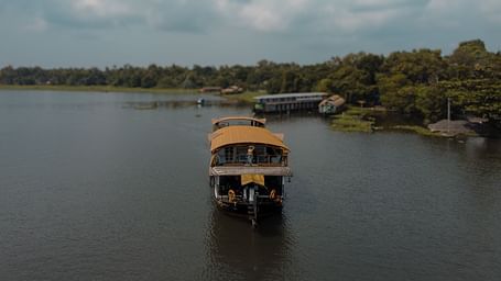 A cruise sailing across the Vembanad Lake with lush greenery in the background - BluSalzz Villas - Muhamma Resort, Alleppey