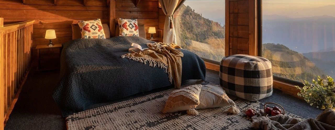 An image of a attic room with king size bed with a huge window providing a view of mountains - Avalon Cottages, Kanatal