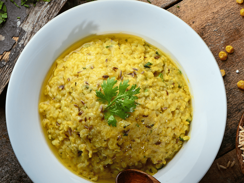 A white bowl of yellow kitchari garnished with coriander leaves on a wooden table