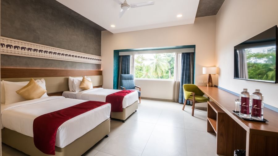 A wide view of a hotel room with two beds, a desk, and a window offering natural light at Shilton Dee Cee.