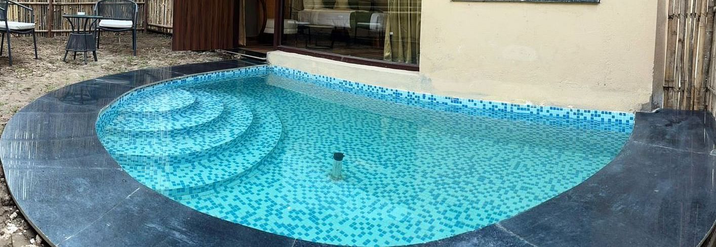 Luxury Villa with Plunge Pool featuring a private outdoor pool with steps leading into the water is surrounded by dark stone and lush greenery at The Qualia Resort Club & Brewery, Udaipur.