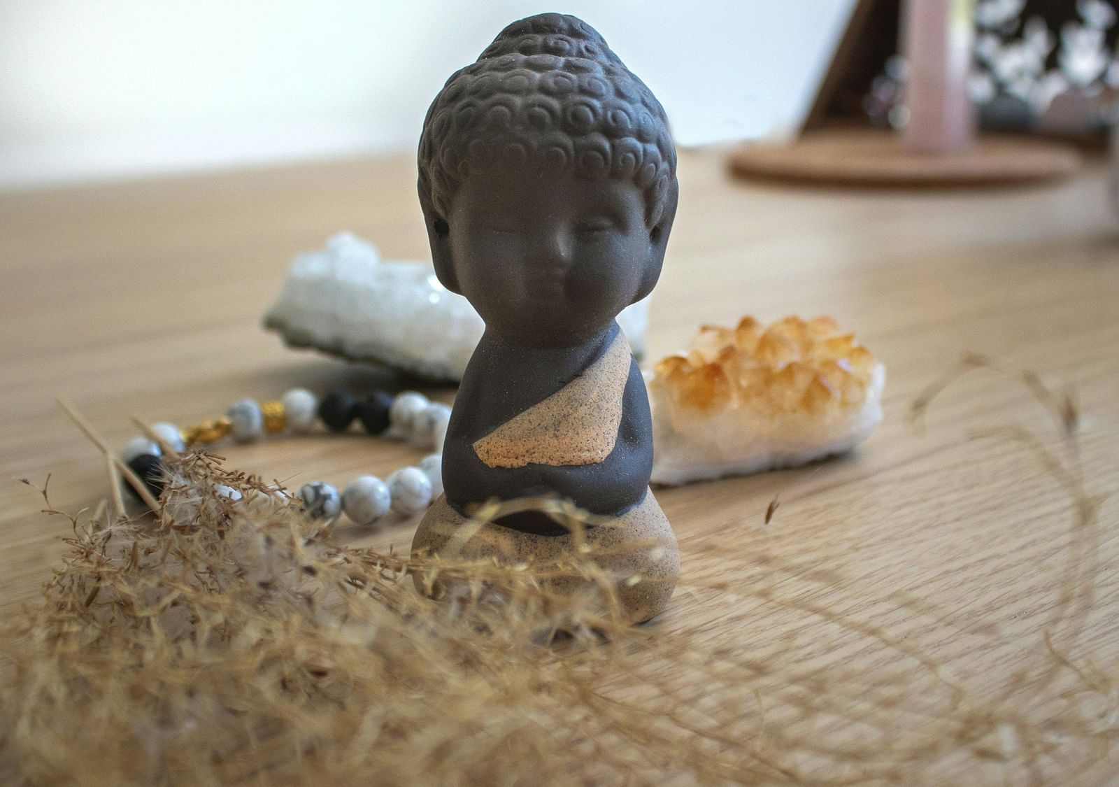 A Buddha sculpture placed on a wooden table along with a crystal bracelet, dry herbs, and crystals