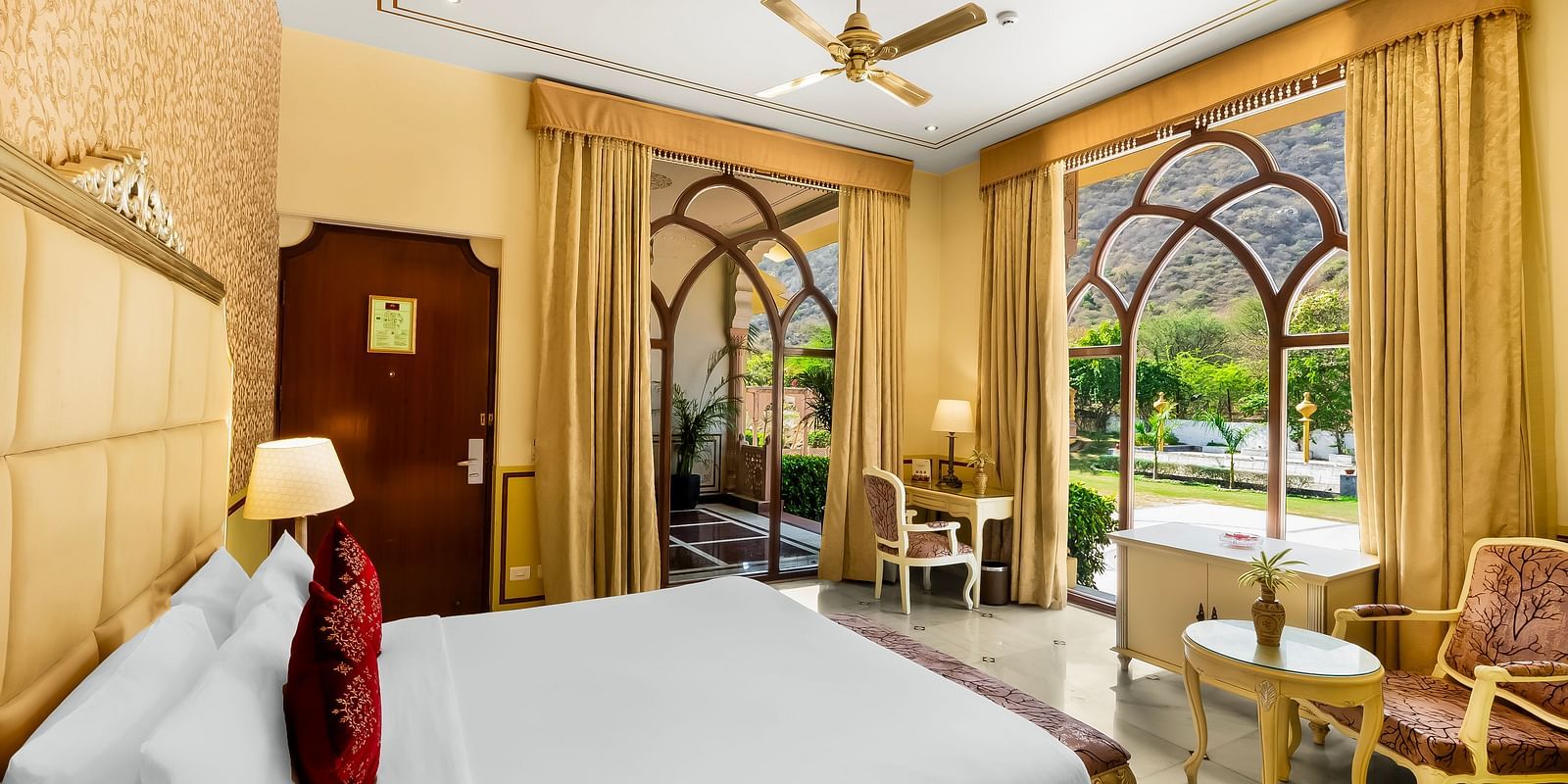 Luxurious suite at Rajasthali Resort Jaipur featuring canopy bed, royal seating area, and grand arched windows.