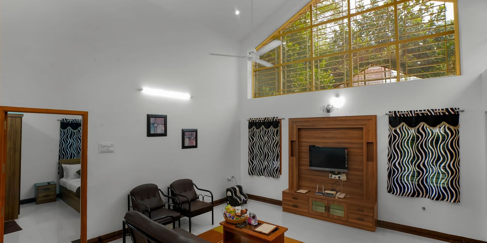 Living room with a sofa and wall-mounted television with a wooden cupboard at WOW Bungalow, Yercaud.