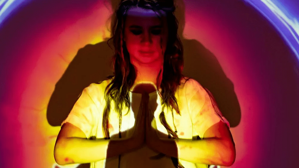 A woman meditating with her eyes closed and colourful halo projected over her.