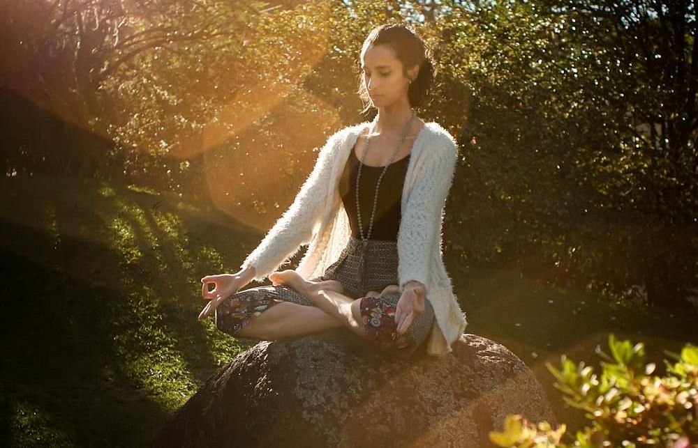 a girl meditating on a rock in a forest on a sunny day