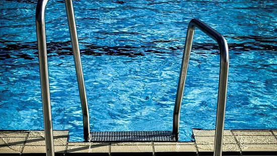 Close-up of metal steps leading into a shimmering blue swimming pool from a paved edge.