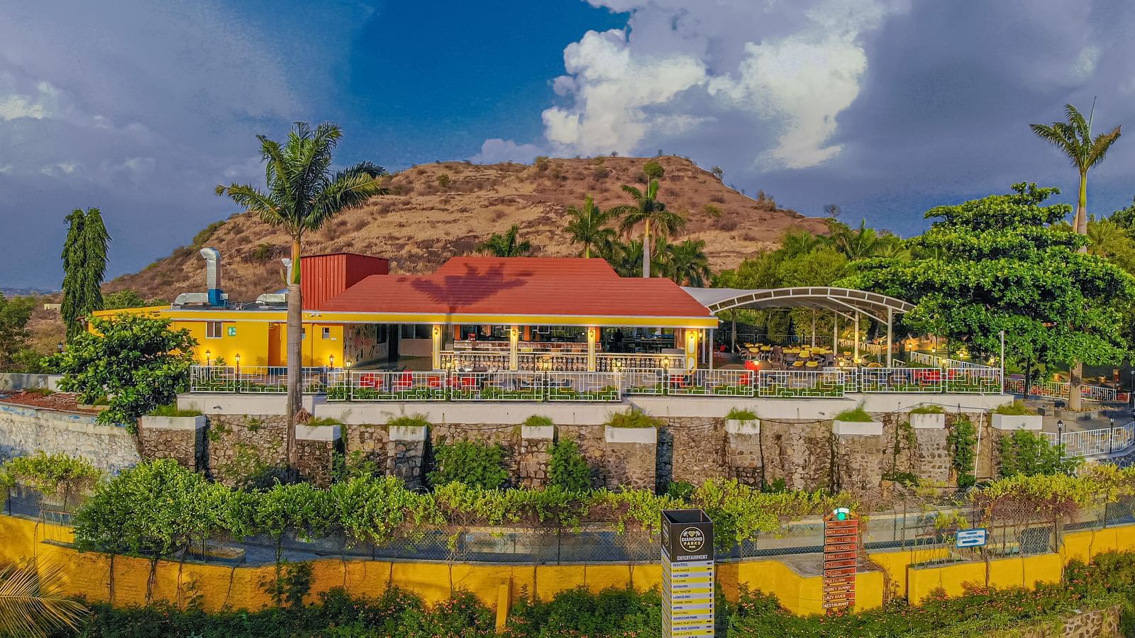 A picture of the cafe encircled by a hill, palm trees, and a round pathway leading to the entrance | Diamond Parks, Pune