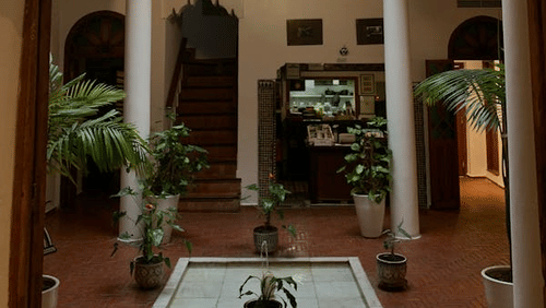 An interior courtyard with arched openings, columns, plants, and a hanging light fixture.