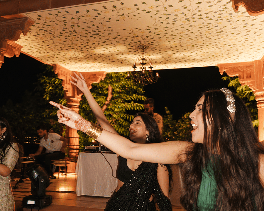 Woman in a green dress dancing and celebrating under an illuminated outdoor poolside at night at Umaid Palace.