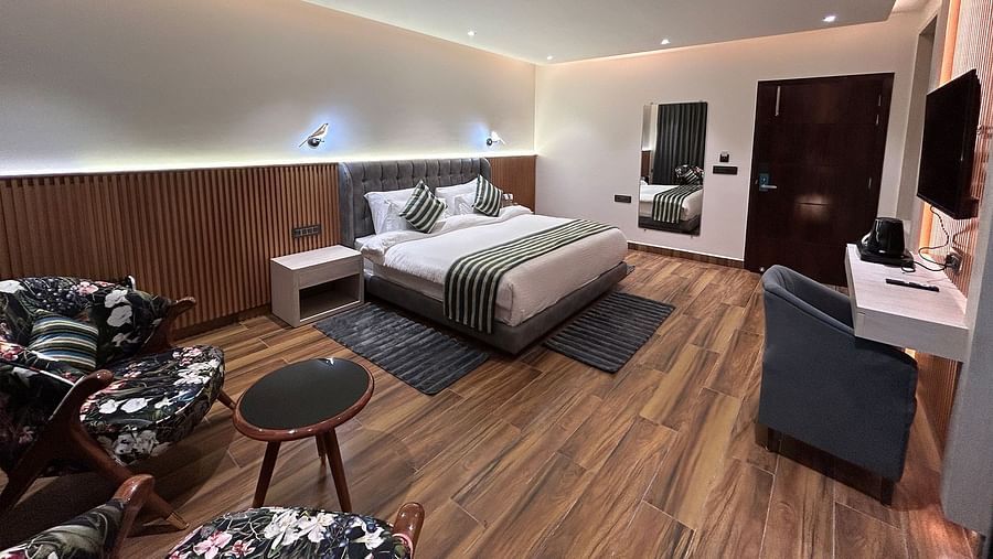 A shot of the deluxe room featuring a bed, bed side tables, two chairs, coffee table, work desk, a couch, a flat screen TV, and a full length mirror - DLS The Emerald, Nainital