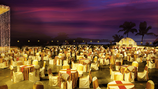 A large outdoor event setup with round tables and chairs covered in cloth arranged under evening lighting.