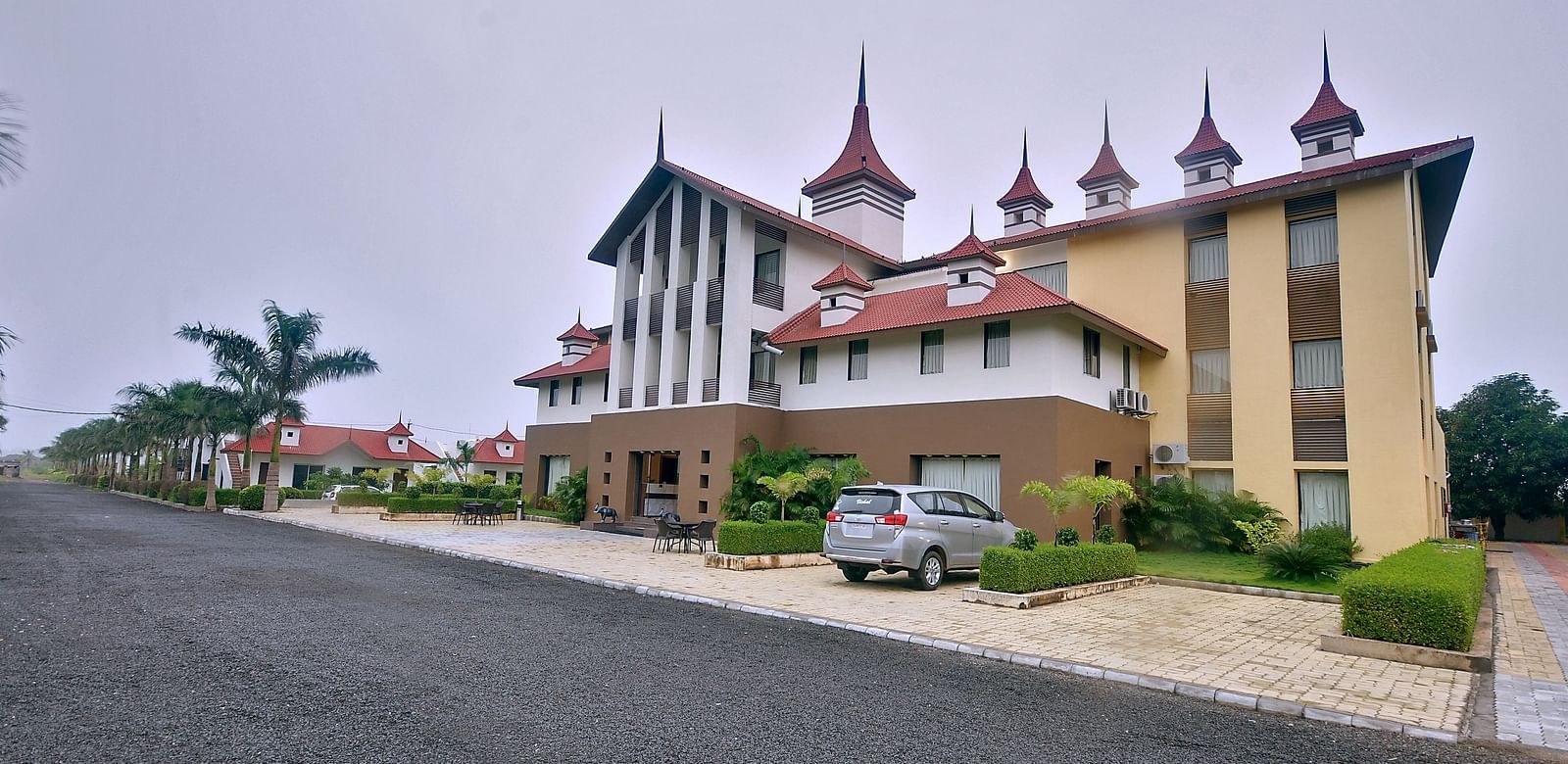 Daytime view of the facade of our hotel with manicured gardens and a vehicle parked right at the front of it - Vishal Lords Inn Gir Forest