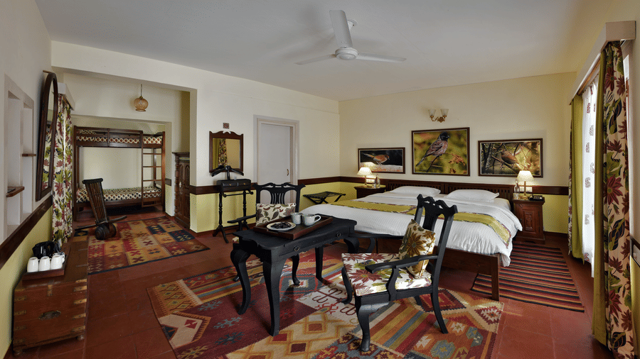 Generous bedroom featuring multiple beds wooden furniture patterned rugs and open layout providing convenience at Neemrana’s Glasshouse on The Ganges for families or group travellers