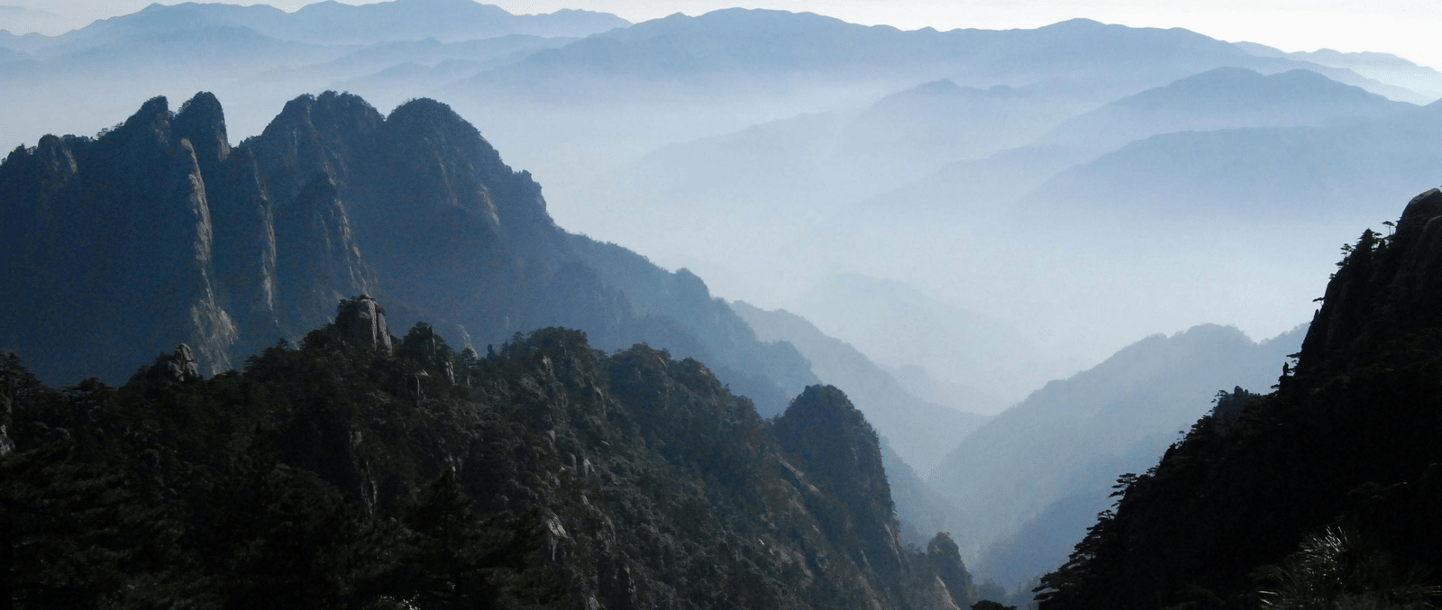 A breathtaking mountain view with layered ridges fading into the distance, framed by dense forest in the foreground