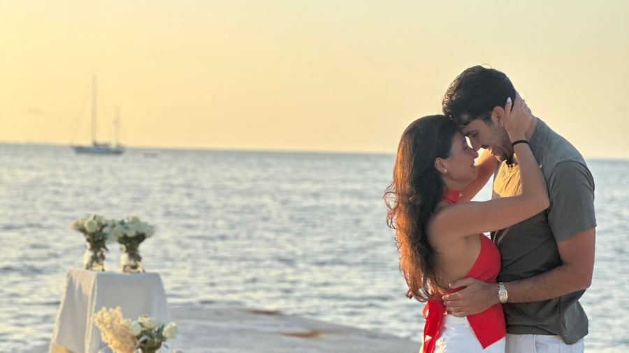 A couple kissing on a white dock with small floral decorations and sailboats on the water during sunset at Casa Morada.
