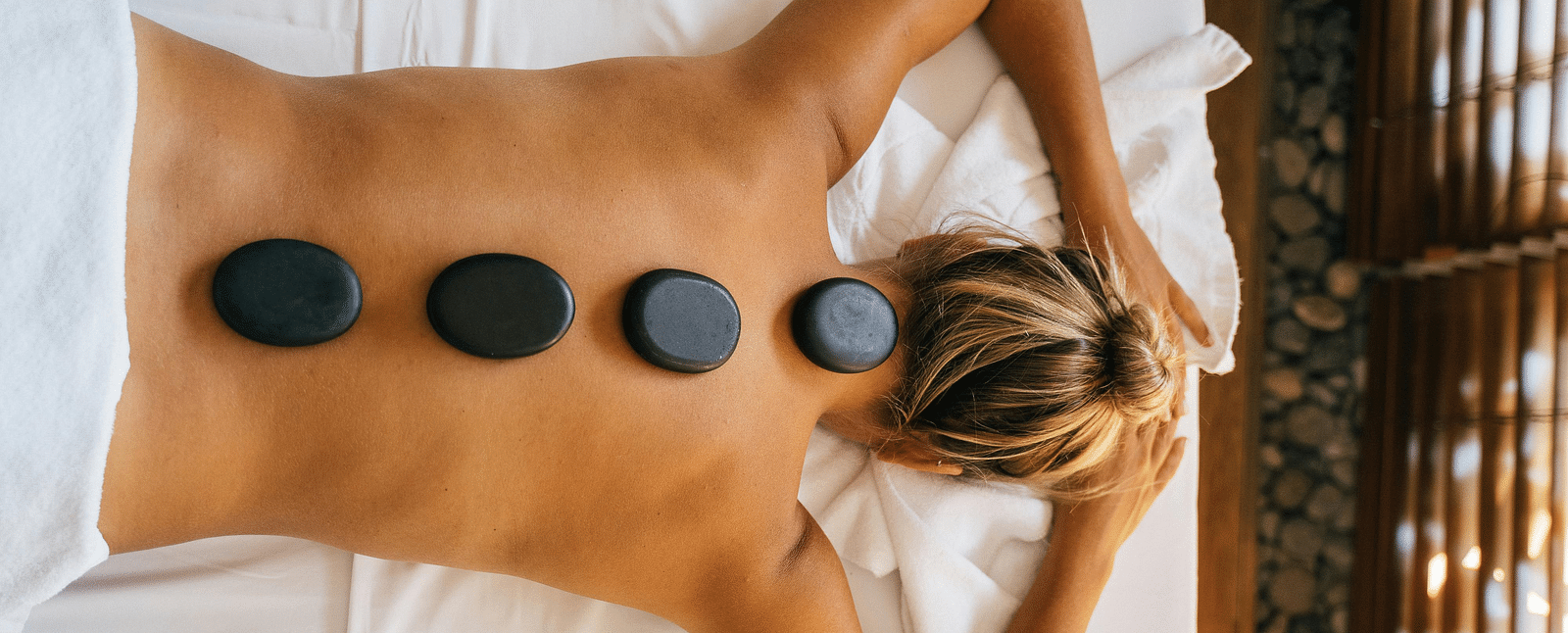 A woman lying down with back with black stones kept over her spine