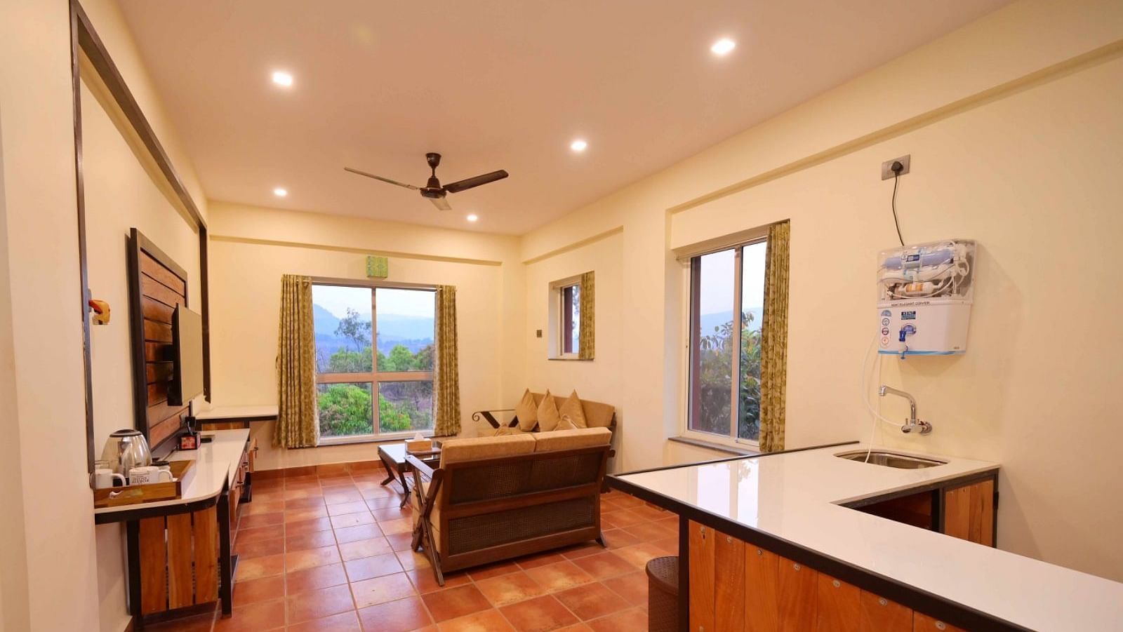 A room with a tan sofa, a desk, a fan on the ceiling, and a door leading outside.