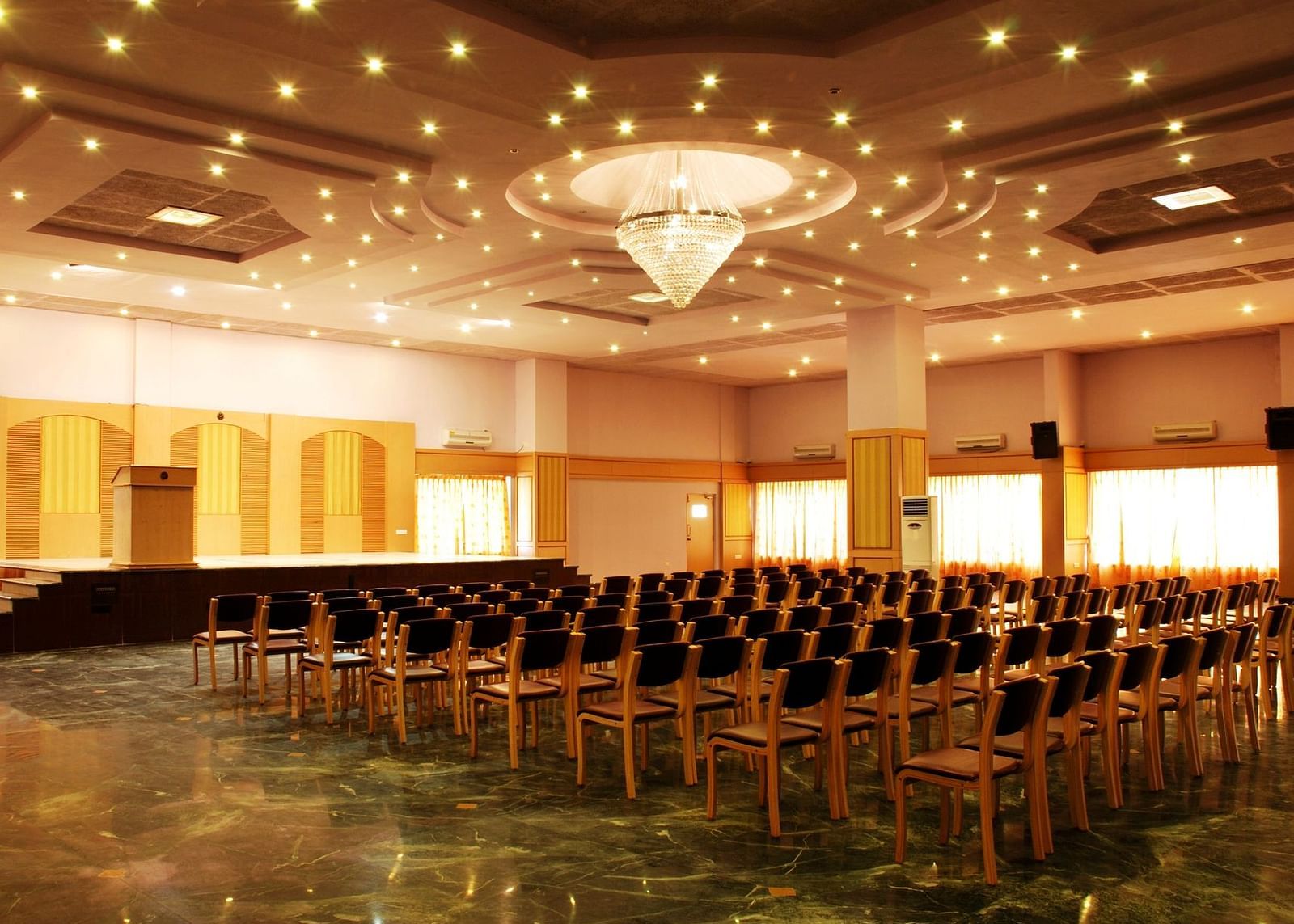 A view of a banquet hall at Paradise Isle Beach Resort, Udupi with a chandelier and a theatre style seating arrangement
